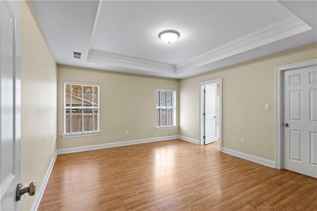 empty room featuring ornamental molding, a tray ceiling, and light hardwood / wood-style flooring