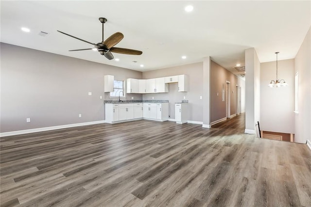 unfurnished living room featuring sink, ceiling fan with notable chandelier, and dark wood-type flooring