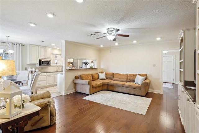 living room with ornamental molding, dark wood-type flooring, ceiling fan with notable chandelier, and a textured ceiling