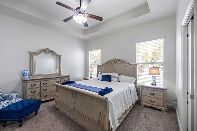 carpeted bedroom with multiple windows, ceiling fan, and a tray ceiling