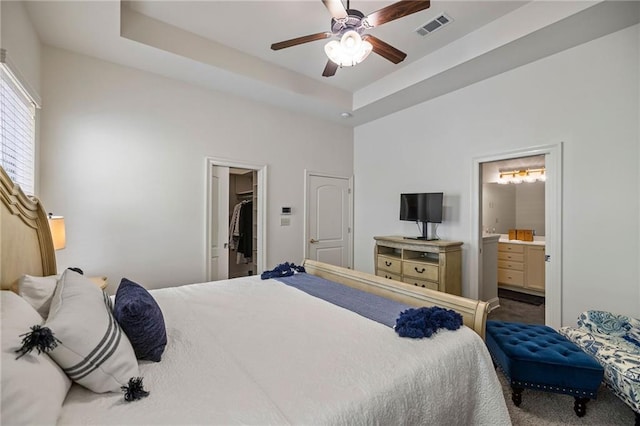 carpeted bedroom with ceiling fan, ensuite bath, a spacious closet, and a raised ceiling