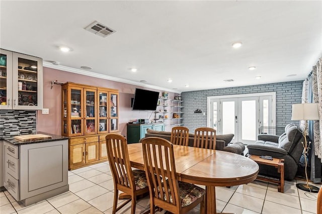 dining area with crown molding, brick wall, light tile patterned floors, and french doors