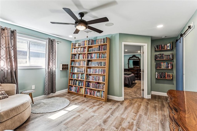 sitting room with ceiling fan, a barn door, and light wood-type flooring