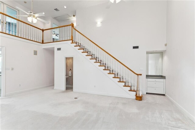 unfurnished living room with ceiling fan, carpet, and a towering ceiling