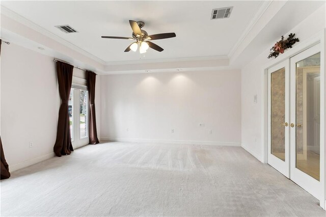 spare room featuring light carpet, a tray ceiling, ornamental molding, and french doors