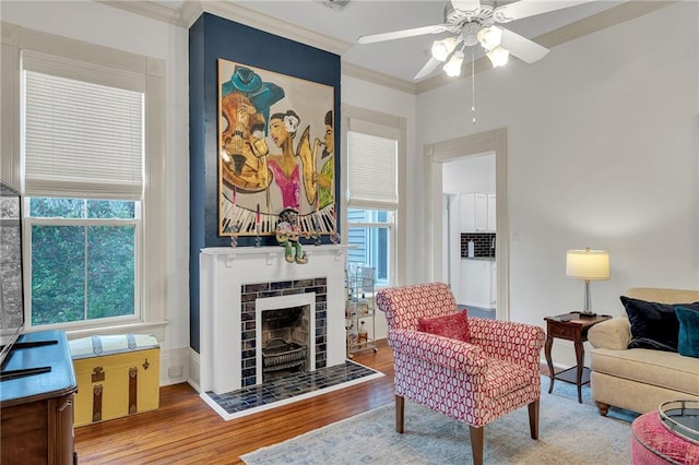 living room with hardwood / wood-style flooring, crown molding, ceiling fan, and a tile fireplace