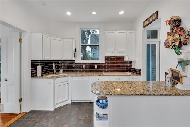 kitchen with light stone counters, dishwasher, sink, and white cabinets