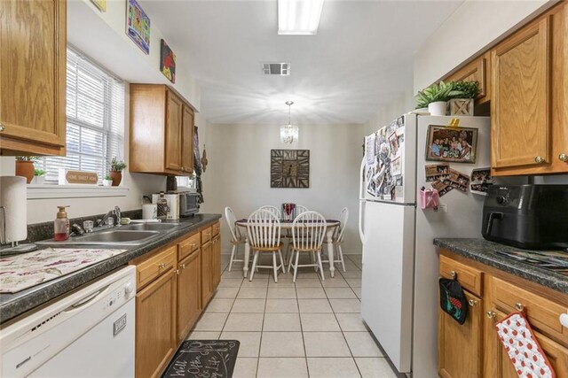 kitchen with sink, white appliances, hanging light fixtures, light tile patterned flooring, and a chandelier