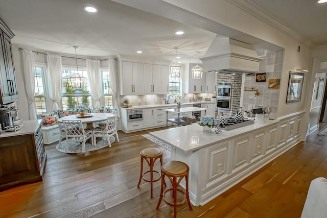 kitchen featuring hanging light fixtures, white cabinetry, custom exhaust hood, and a kitchen breakfast bar