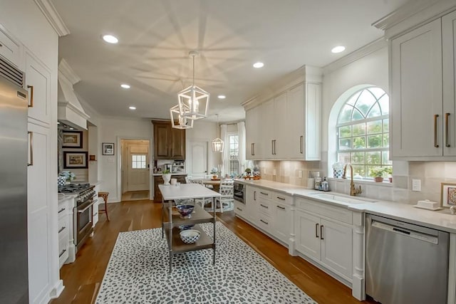 kitchen with sink, hanging light fixtures, backsplash, high quality appliances, and white cabinets