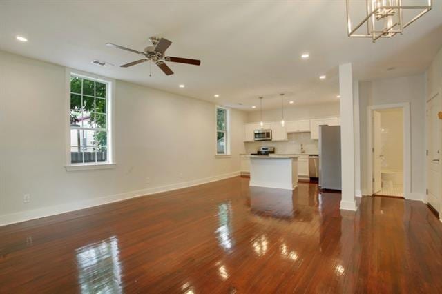 unfurnished living room featuring dark hardwood / wood-style floors and ceiling fan with notable chandelier