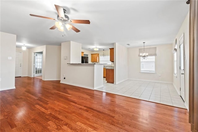 unfurnished living room featuring a wealth of natural light, ceiling fan with notable chandelier, and light wood-type flooring