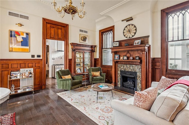 living room featuring a tiled fireplace, ornamental molding, dark wood-type flooring, and an inviting chandelier