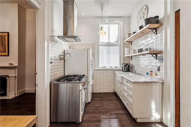 kitchen with pendant lighting, island range hood, stainless steel gas range oven, light stone countertops, and white cabinets