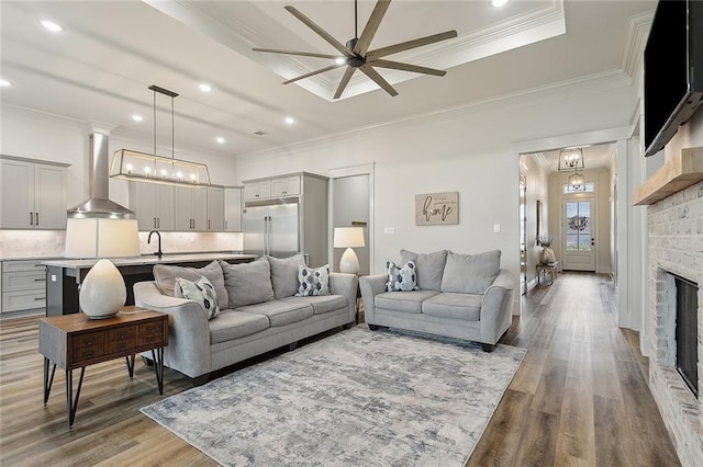 living room with crown molding, ceiling fan with notable chandelier, sink, and hardwood / wood-style floors