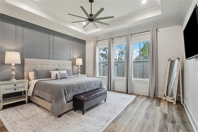 bedroom with crown molding, light wood-type flooring, and a tray ceiling