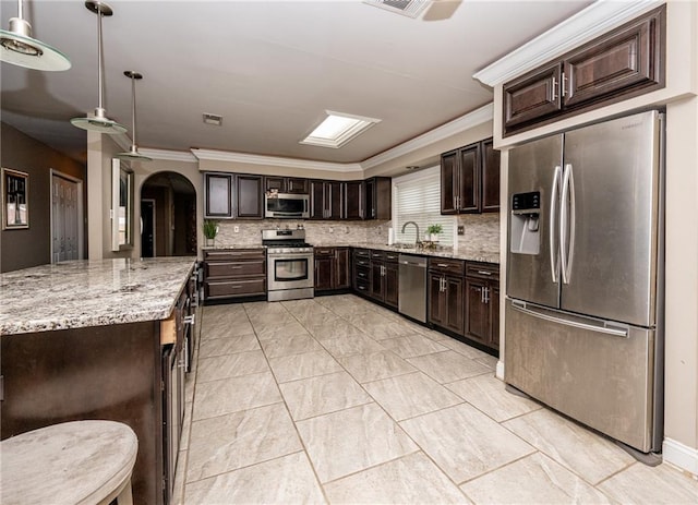 kitchen with appliances with stainless steel finishes, sink, hanging light fixtures, light stone countertops, and dark brown cabinets