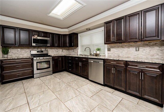 kitchen with sink, appliances with stainless steel finishes, dark brown cabinetry, light stone counters, and decorative backsplash