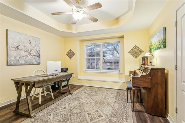 office space featuring a raised ceiling, hardwood / wood-style flooring, and ceiling fan