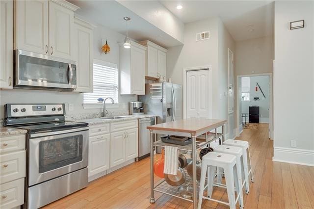 kitchen with sink, white cabinets, hanging light fixtures, stainless steel appliances, and light wood-type flooring