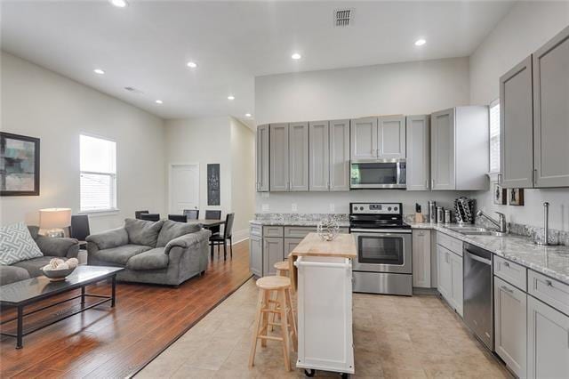 kitchen with gray cabinetry, a kitchen bar, a center island, stainless steel appliances, and light stone countertops