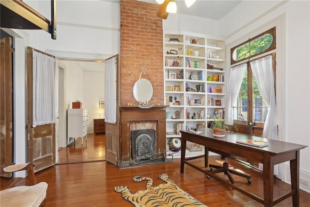 home office featuring hardwood / wood-style flooring, a brick fireplace, and ceiling fan