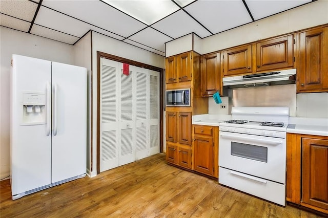 kitchen featuring white appliances, light wood finished floors, brown cabinets, light countertops, and under cabinet range hood