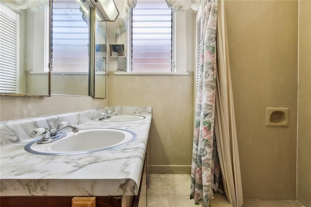 full bathroom featuring double vanity, tile patterned flooring, a sink, and baseboards