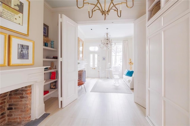 hall with ornamental molding, built in features, an inviting chandelier, and light hardwood / wood-style floors