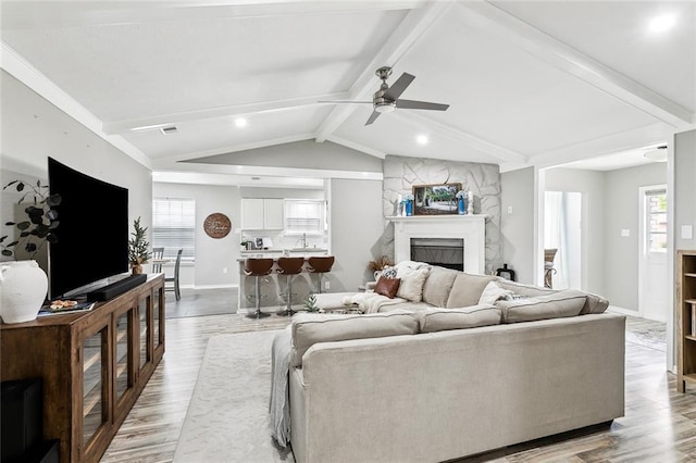 living room featuring sink, lofted ceiling with beams, light hardwood / wood-style flooring, a large fireplace, and ceiling fan