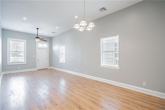 empty room with ceiling fan with notable chandelier and light hardwood / wood-style floors