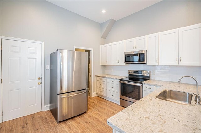 kitchen with sink, light stone counters, light wood-type flooring, appliances with stainless steel finishes, and white cabinets