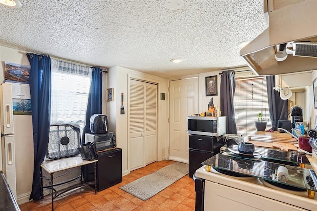 kitchen featuring stove, a textured ceiling, a healthy amount of sunlight, and refrigerator