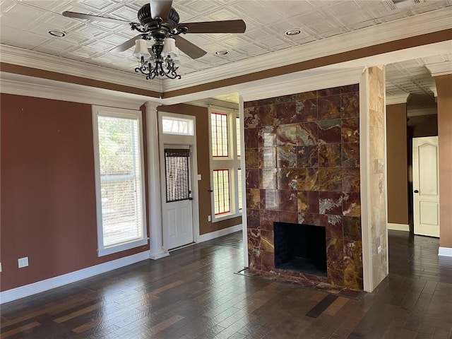 unfurnished living room with crown molding, dark hardwood / wood-style flooring, ceiling fan, decorative columns, and a tiled fireplace