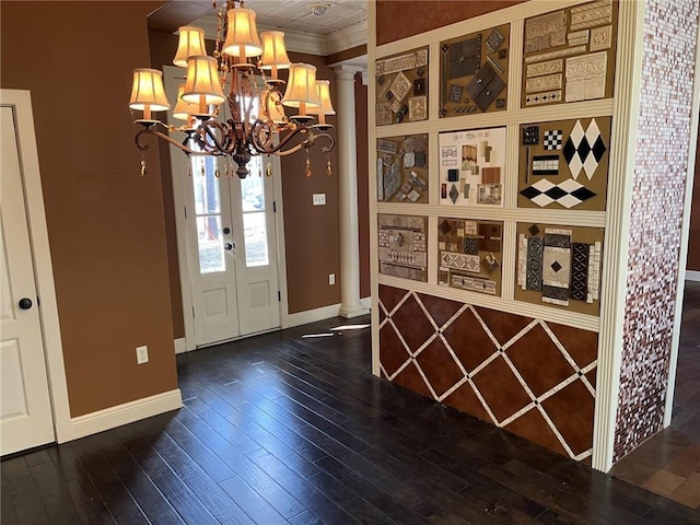 entrance foyer featuring ornate columns, dark hardwood / wood-style floors, a notable chandelier, crown molding, and french doors