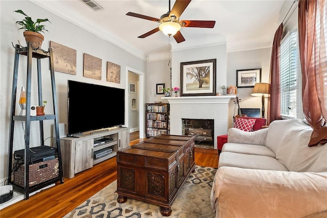 living room with crown molding, dark wood-type flooring, ceiling fan, and a fireplace