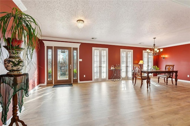 foyer featuring visible vents, crown molding, light wood-style flooring, french doors, and a notable chandelier