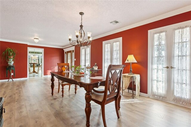 dining room featuring ornamental molding, light hardwood / wood-style floors, french doors, and a textured ceiling