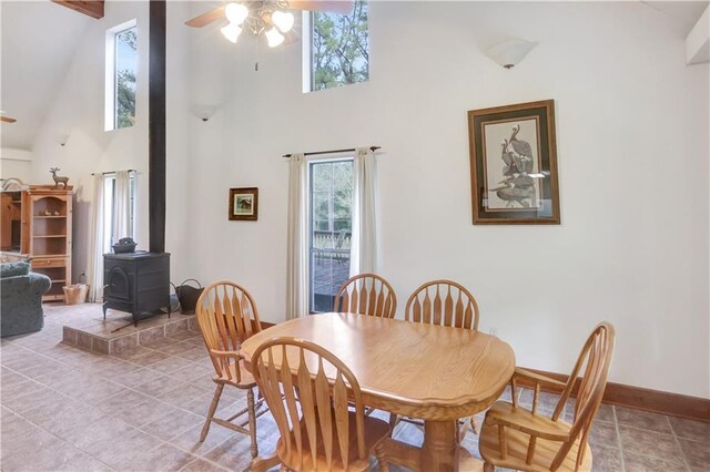 dining area featuring a high ceiling, light tile patterned flooring, ceiling fan, and a wood stove