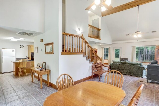 dining area featuring high vaulted ceiling, ceiling fan, and a wood stove