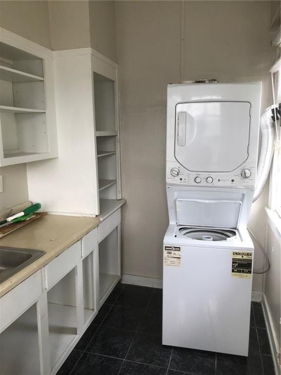 laundry area featuring stacked washer / drying machine, sink, and dark tile patterned flooring