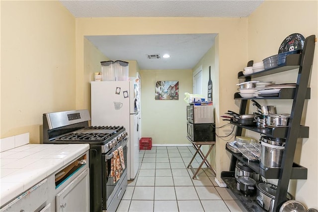 kitchen featuring white cabinetry, stainless steel range with gas cooktop, tile countertops, and light tile patterned flooring