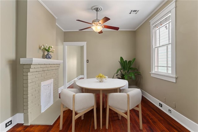 dining room featuring a brick fireplace, crown molding, dark wood-type flooring, and ceiling fan