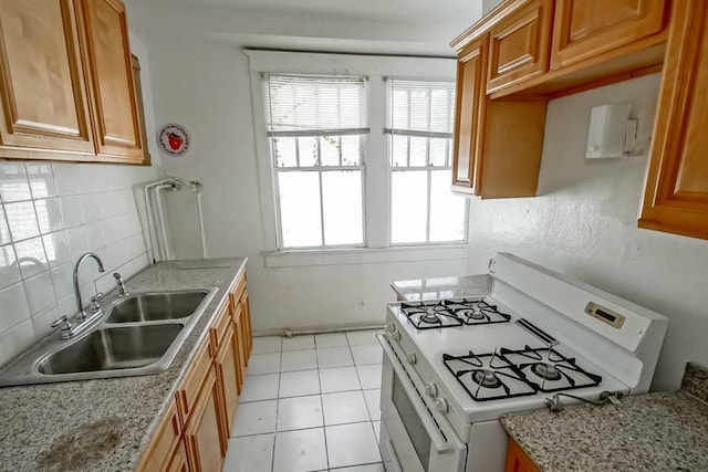 kitchen featuring light stone counters, sink, white range with gas stovetop, and a wealth of natural light