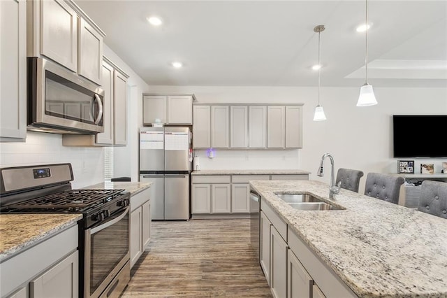 kitchen featuring sink, decorative light fixtures, light hardwood / wood-style flooring, stainless steel appliances, and a kitchen island with sink