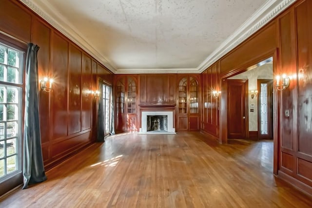 unfurnished living room featuring crown molding, wooden walls, and light hardwood / wood-style flooring