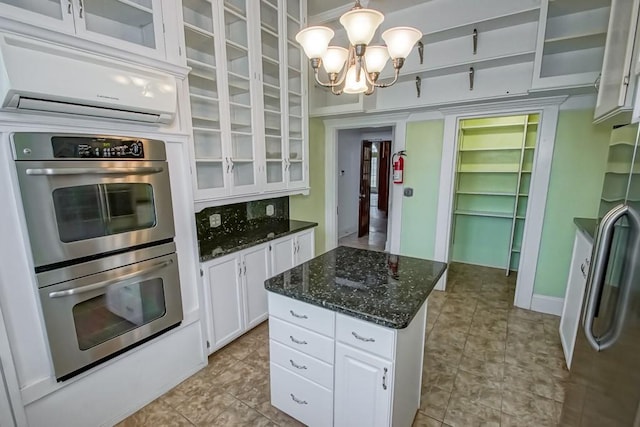 kitchen featuring appliances with stainless steel finishes, hanging light fixtures, white cabinets, an AC wall unit, and a chandelier