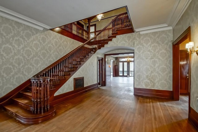 staircase featuring wood-type flooring, ornamental molding, and a chandelier