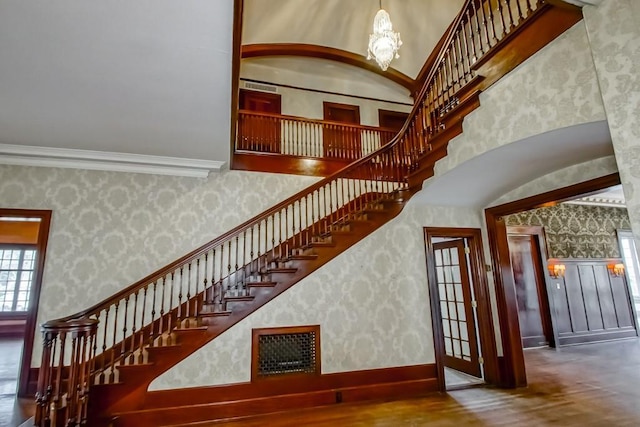 stairs with crown molding, a chandelier, hardwood / wood-style floors, and a high ceiling