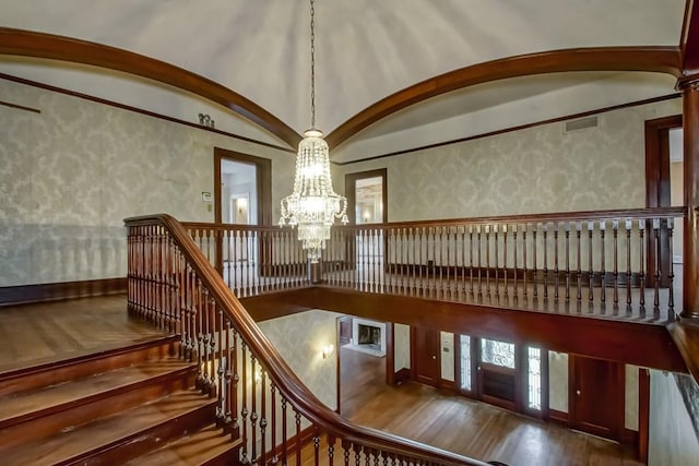 staircase with wood-type flooring, a chandelier, and vaulted ceiling